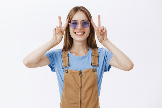 Ragazza attraente felice ottimista che mostra gesto di pace e sorridente spensierato