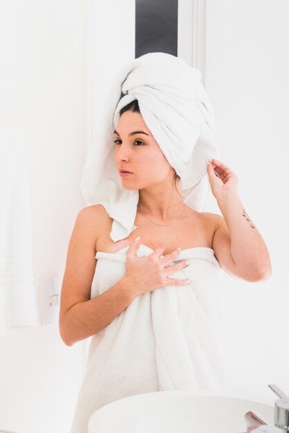 Ragazza avvolta i capelli e il corpo in un asciugamano guardando nello specchio