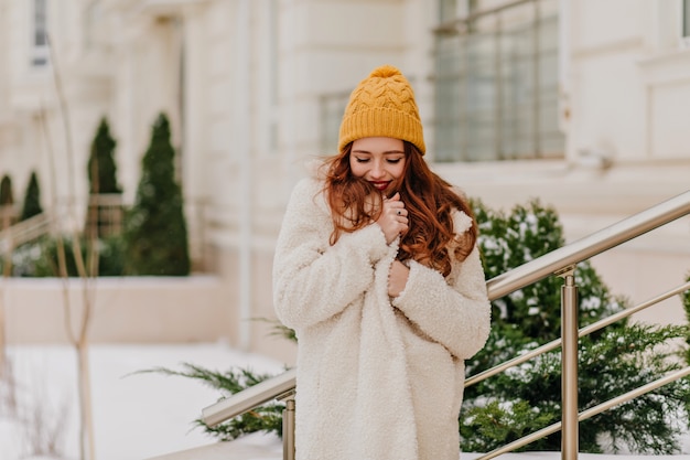 Ragazza bianca Jocund in posa in inverno. Amabile giovane signora in piedi vicino a verde abete.