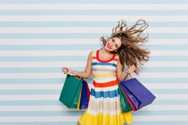 Ragazza bianca spensierata con lunghi capelli ricci che si gode lo shopping prima delle vacanze. La bella signora dai capelli scuri ha comprato regali per il nuovo anno ed è felice per questo.