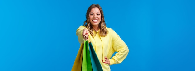 Ragazza bionda allegra che ti dà borse della spesa e regali d'acquisto felici sorridenti per le vacanze in famiglia