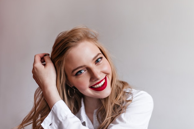 Ragazza bionda allegra con le labbra rosse. Sorridente giovane donna europea in posa in camicia bianca.