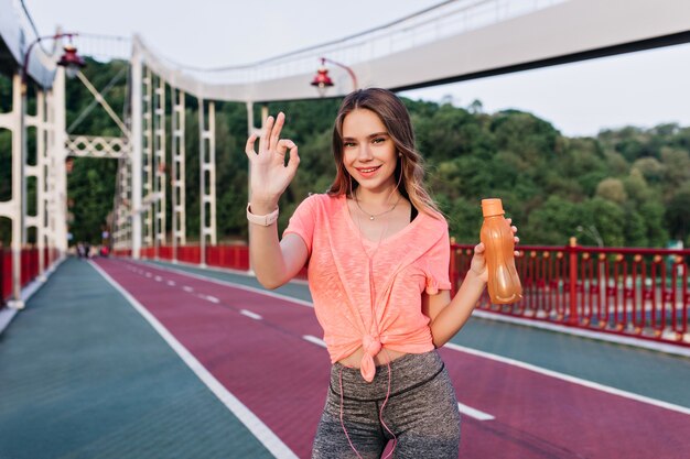 Ragazza bionda attiva trascorrere del tempo allo stadio. Corridore femminile carino in posa dopo la maratona e sorridente.