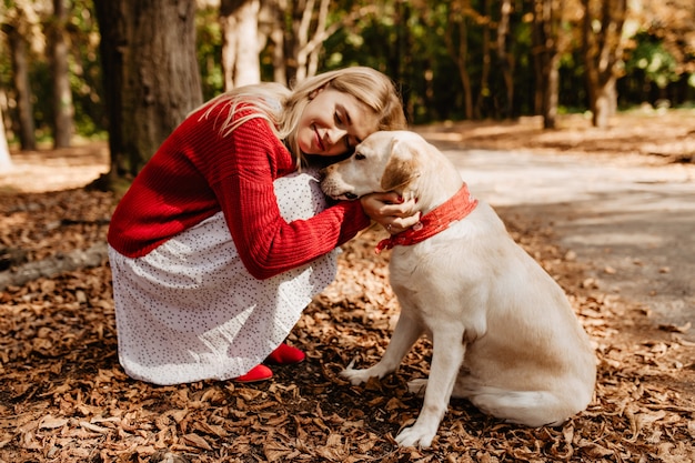 Ragazza bionda beatamente felice che sorride vicino al suo cane. Bella donna che si sente felice con l'amato animale domestico.