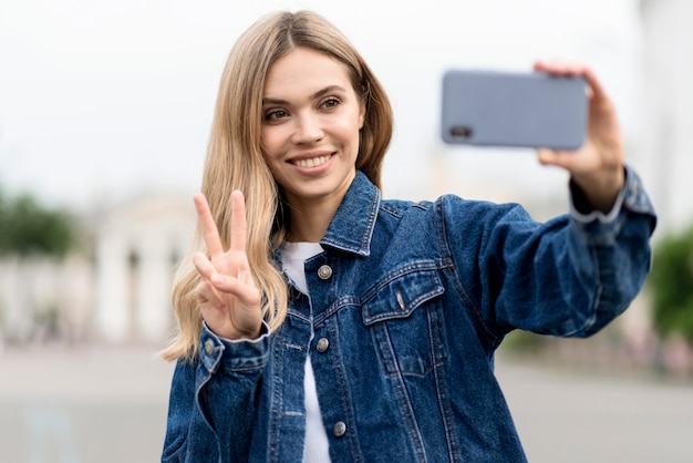 Ragazza bionda carina che cattura una foto di auto e che tiene il segno di pace