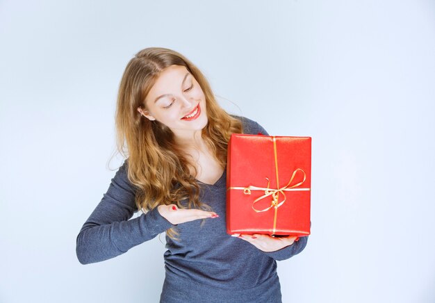 Ragazza bionda che abbraccia la sua confezione regalo rossa e si sente felice.