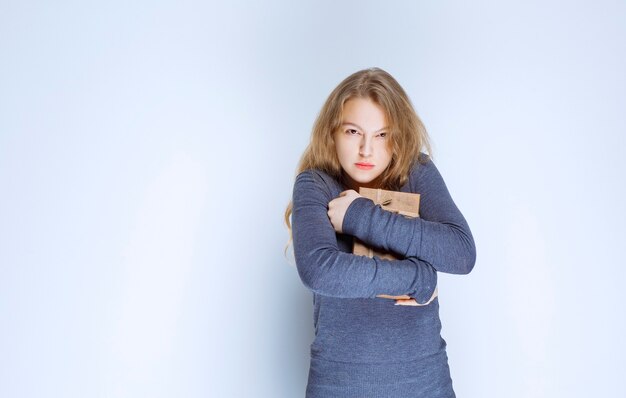 Ragazza bionda che abbraccia stretto il suo contenitore di regalo di cartone.