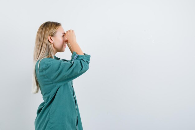 Ragazza bionda che guarda attraverso le dita in camicetta verde e sembra concentrata.