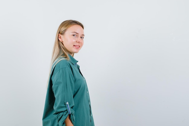 Ragazza bionda che guarda sopra la spalla in camicetta verde e sembra incantevole