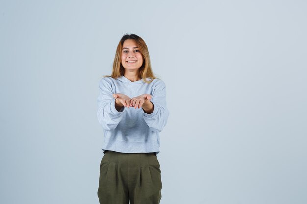 Ragazza bionda che invita a venire in felpa e pantaloni blu verde oliva e sembra amabile. vista frontale.