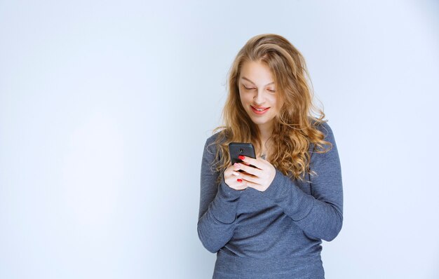 Ragazza bionda che manda SMS e invia messaggi con il suo smartphone.