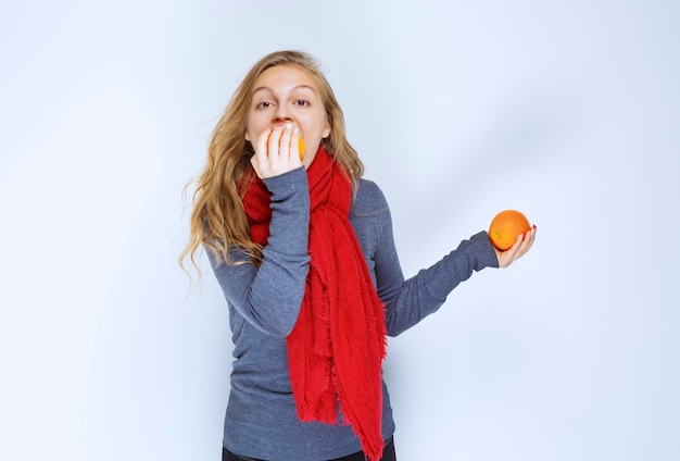 Ragazza bionda che morde un succoso frutto arancione.