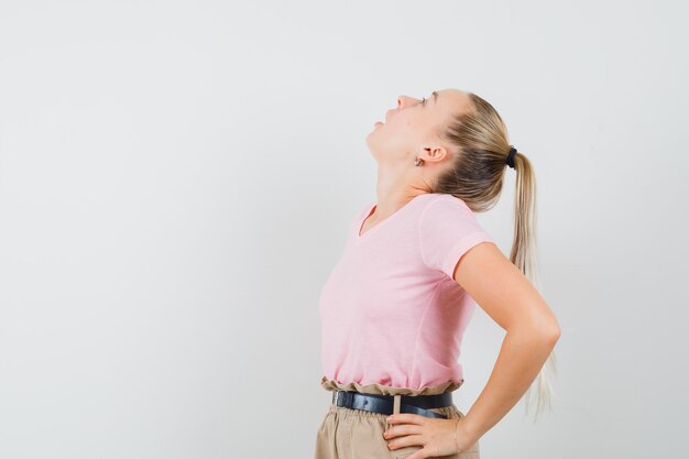 Ragazza bionda che osserva in su in maglietta, pantaloni e che sembra stupita. vista frontale.