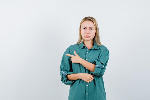 Ragazza bionda che punta a sinistra con il dito indice in camicetta verde e sembra infastidita