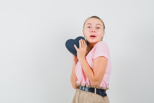 Ragazza bionda che tiene il contenitore di regalo in maglietta, pantaloni e che sembra felice, vista frontale.