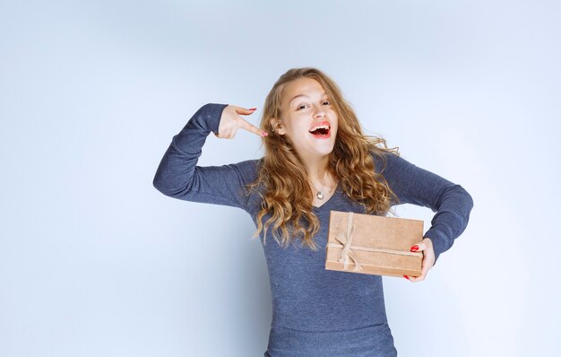 Ragazza bionda che tiene in mano una confezione regalo di cartone e la indica.