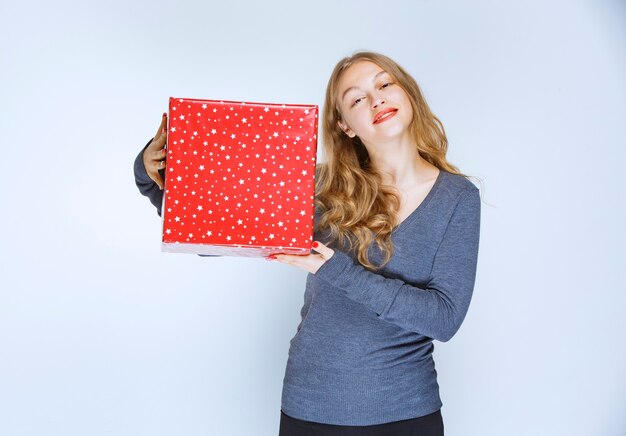 Ragazza bionda che tiene un grande contenitore di regalo rosso.