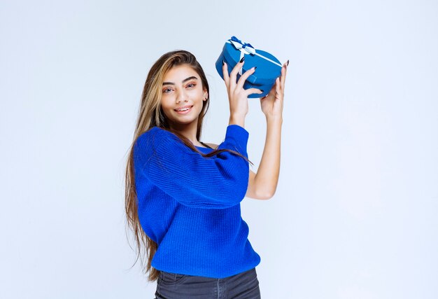 Ragazza bionda che tiene una confezione regalo blu a forma di cuore.