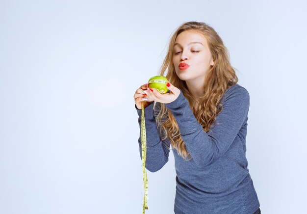 Ragazza bionda che tiene una mela verde nei suoi palmi.