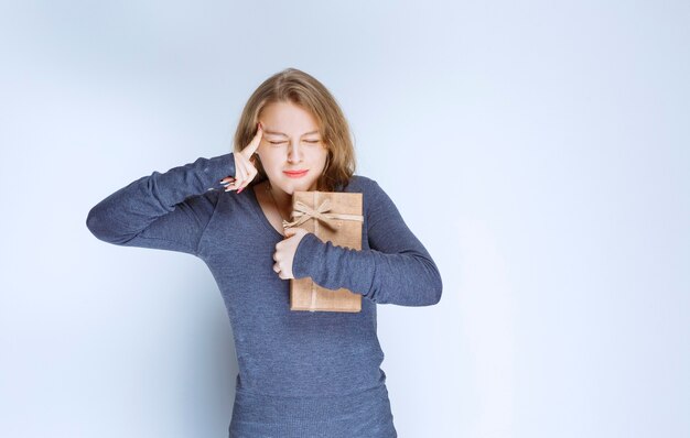 Ragazza bionda che tiene una scatola regalo di cartone e ha un'idea.