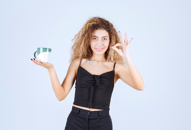 Ragazza bionda che tiene una tazza di caffè e mostra che le è piaciuto il gusto.