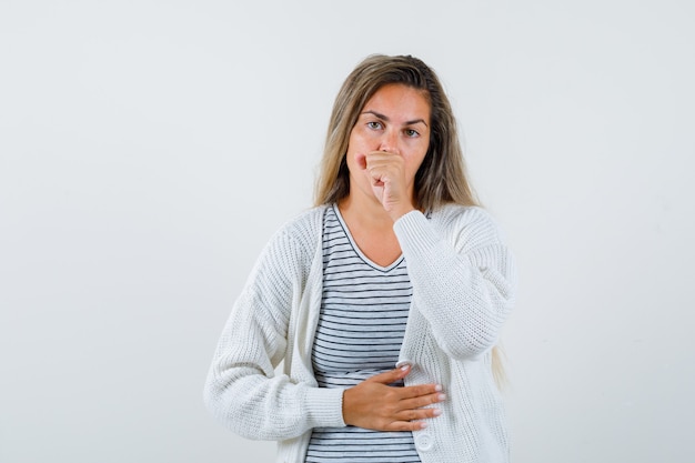 Ragazza bionda che tossisce in maglietta a righe, cardigan bianco e pantaloni di jeans e sembra malata. vista frontale.