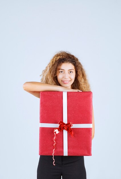 Ragazza bionda con i capelli ricci che tiene in mano una confezione regalo rossa e si sente positiva.