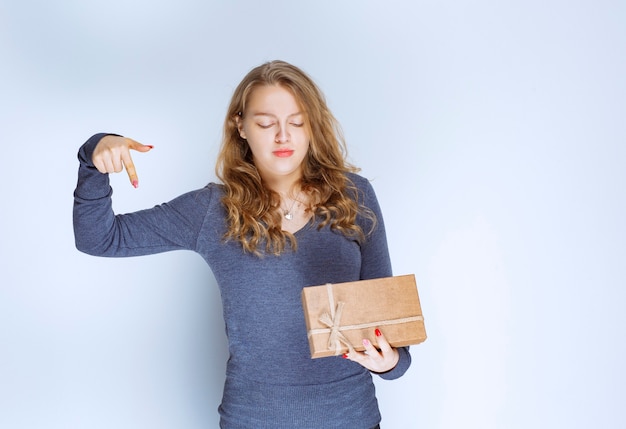 Ragazza bionda con una confezione regalo di cartone che punta sotto.