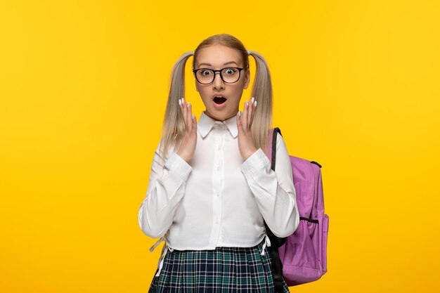 Ragazza bionda della giornata mondiale del libro con le code di cavallo eccitate in uniforme su sfondo giallo