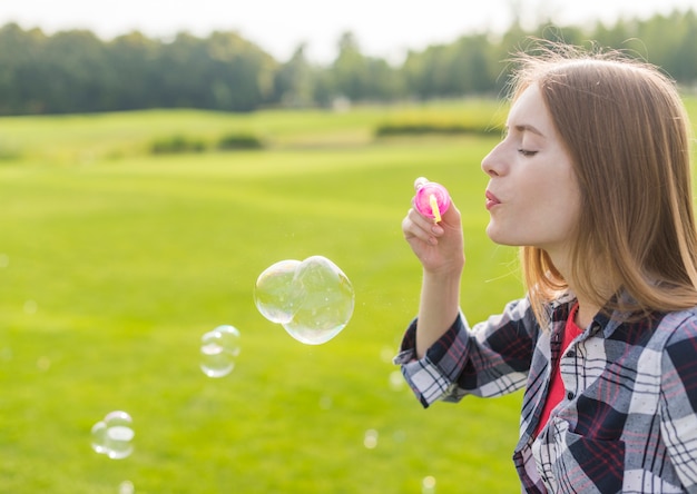 Ragazza bionda di vista laterale che fa le bolle