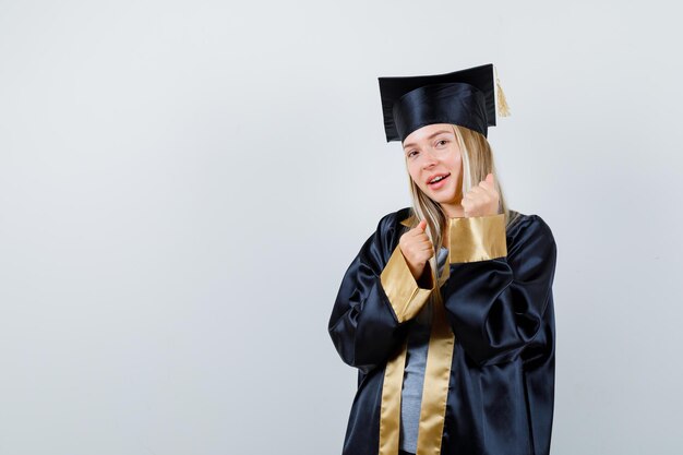 Ragazza bionda in abito da laurea e berretto in piedi in posa da pugile e sembra felice