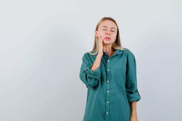 Ragazza bionda in camicetta verde che ha mal di denti e sembra esausta