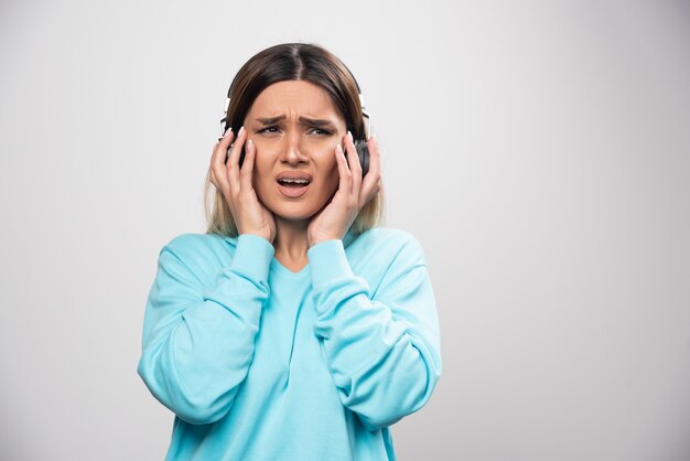 Ragazza bionda in felpa blu ascolta le cuffie e non gode della musica