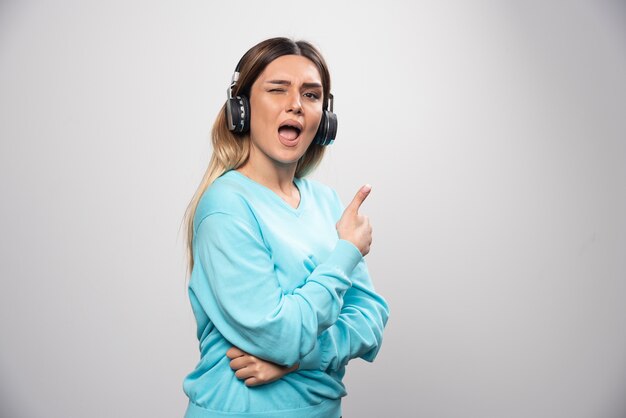 Ragazza bionda in felpa blu che indossa le cuffie, godersi la musica e divertirsi.