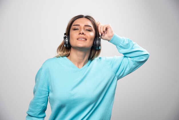 Ragazza bionda in felpa blu che indossa le cuffie, godersi la musica e divertirsi