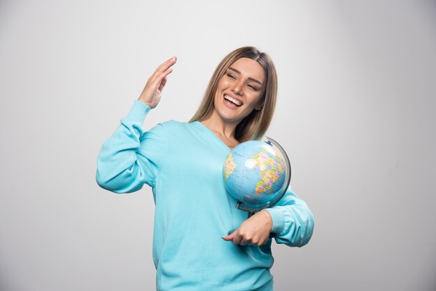 Ragazza bionda in felpa blu che tiene un globo, indovinando la posizione e divertendosi.