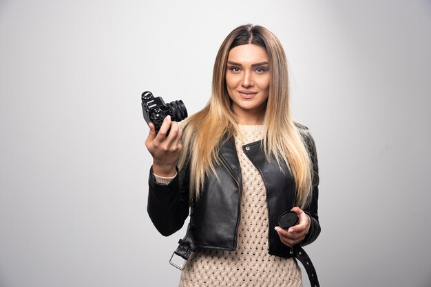 Ragazza bionda in giacca di pelle nera prendendo i suoi selfie con una macchina fotografica.