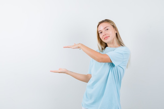 Ragazza bionda in maglietta blu che mostra il gesto delle scale e che sembra carina, vista frontale.