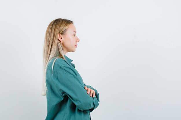 Ragazza bionda in piedi con le braccia incrociate in camicetta verde e sembra raggiante.