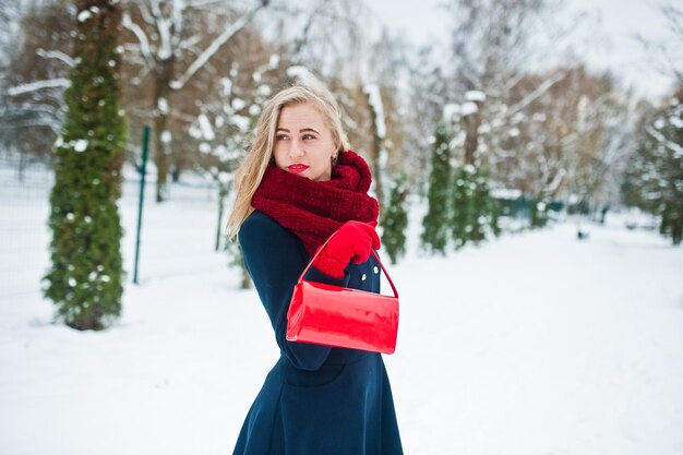 Ragazza bionda in sciarpa rossa e cappotto che cammina al parco il giorno d'inverno