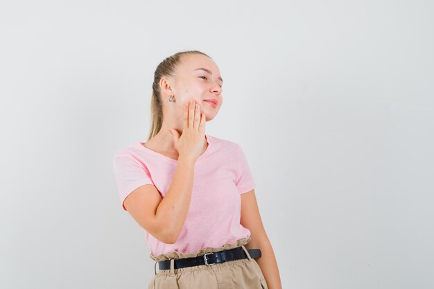 Ragazza bionda in t-shirt, pantaloni che controllano la sua pelle del viso e sembra carina, vista frontale.