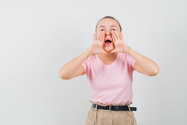 Ragazza bionda in t-shirt, pantaloni che grida o annuncia qualcosa, vista frontale.