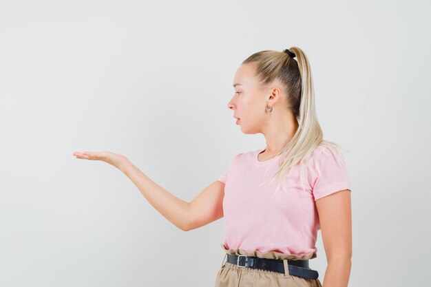 Ragazza bionda in t-shirt, pantaloni che guardano il suo palmo aperto da parte e che sembra concentrata, vista frontale.