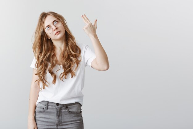 Ragazza bionda infastidita e annoiata che si spara alla testa per l'angoscia, alzando gli occhi al cielo per l'irritazione