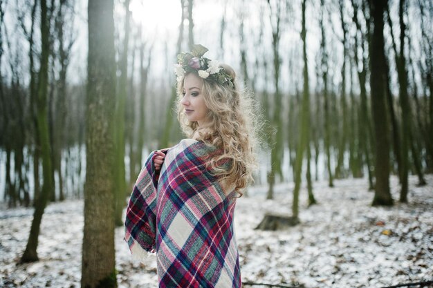 Ragazza bionda riccia carina con corona in plaid a scacchi nella foresta innevata nella giornata invernale