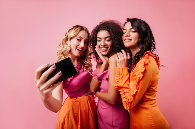 Ragazza bionda romantica che fa selfie con gli amici Belle donne che posano su sfondo rosa