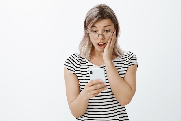 ragazza bionda scioccata e stupita in posa in studio con il suo telefono