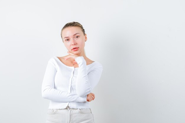 Ragazza bionda sta mettendo la mano sotto il mento su sfondo bianco