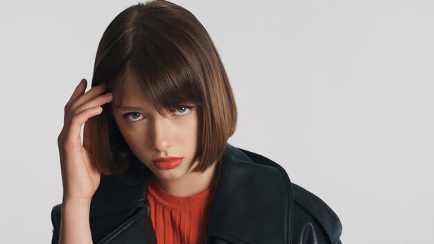 Ragazza bruna sconvolta con capelli bob e labbra rosse che sembrano timide sulla fotocamera isolata su sfondo bianco. Espressione triste