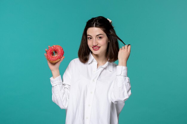 Ragazza carina bella giovane ragazza castana carina in camicia bianca con una ciambella sorridente